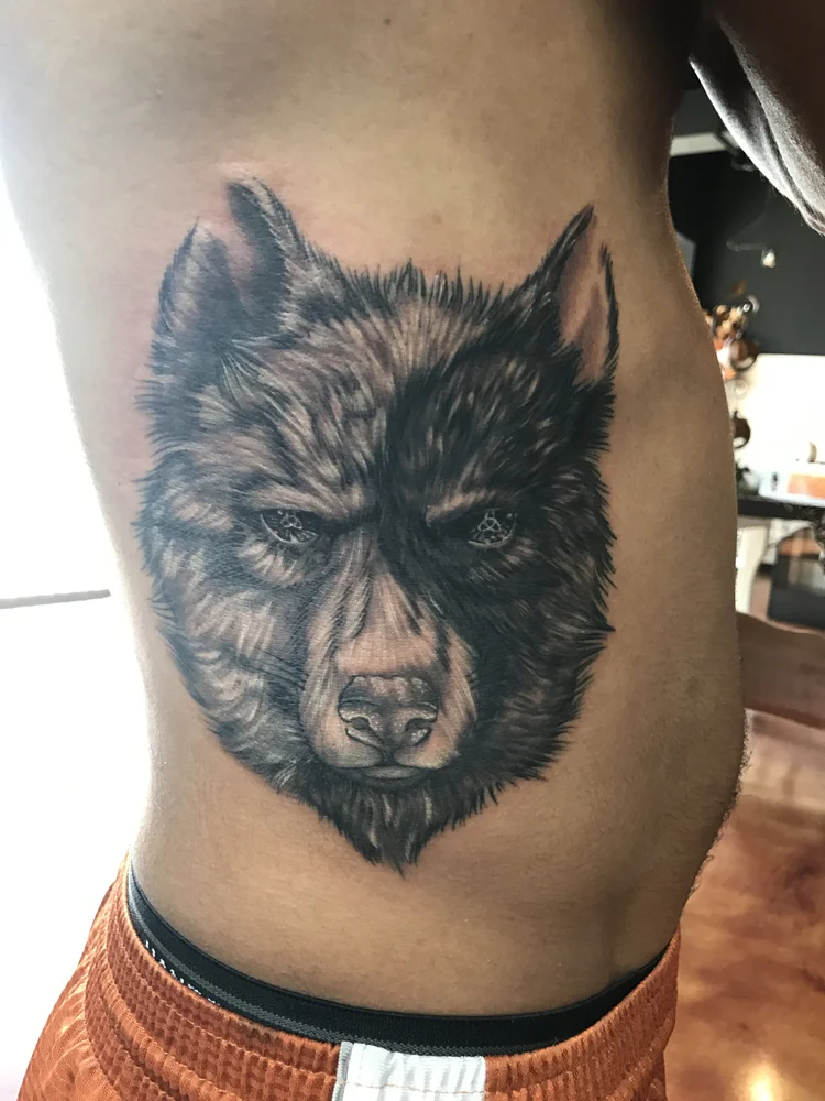 Black and grey wolf portrait tattoo on the ribs
