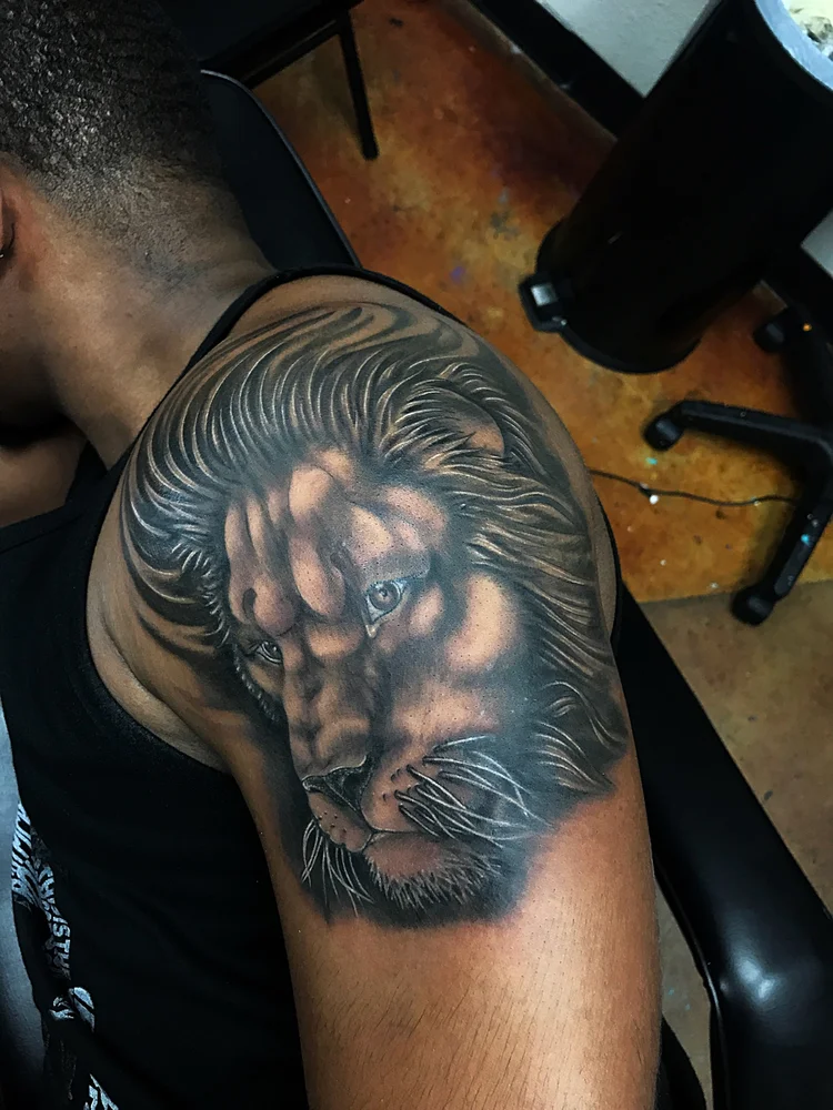 Black and grey lion tattoo on the shoulder