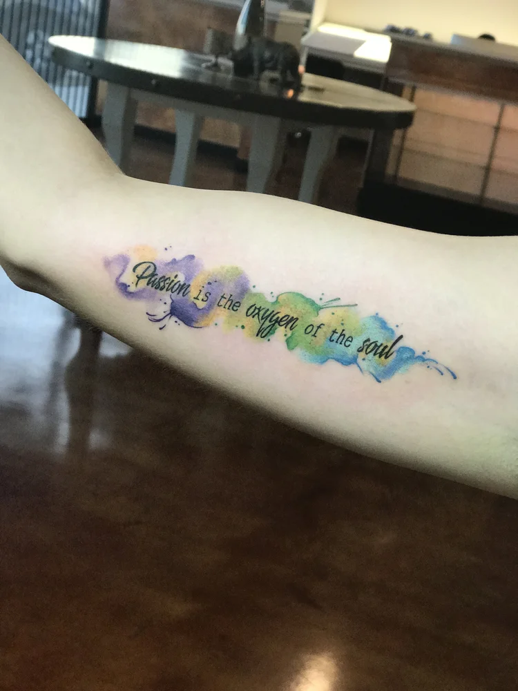 Script lettering with a watercolor wash on the forearm