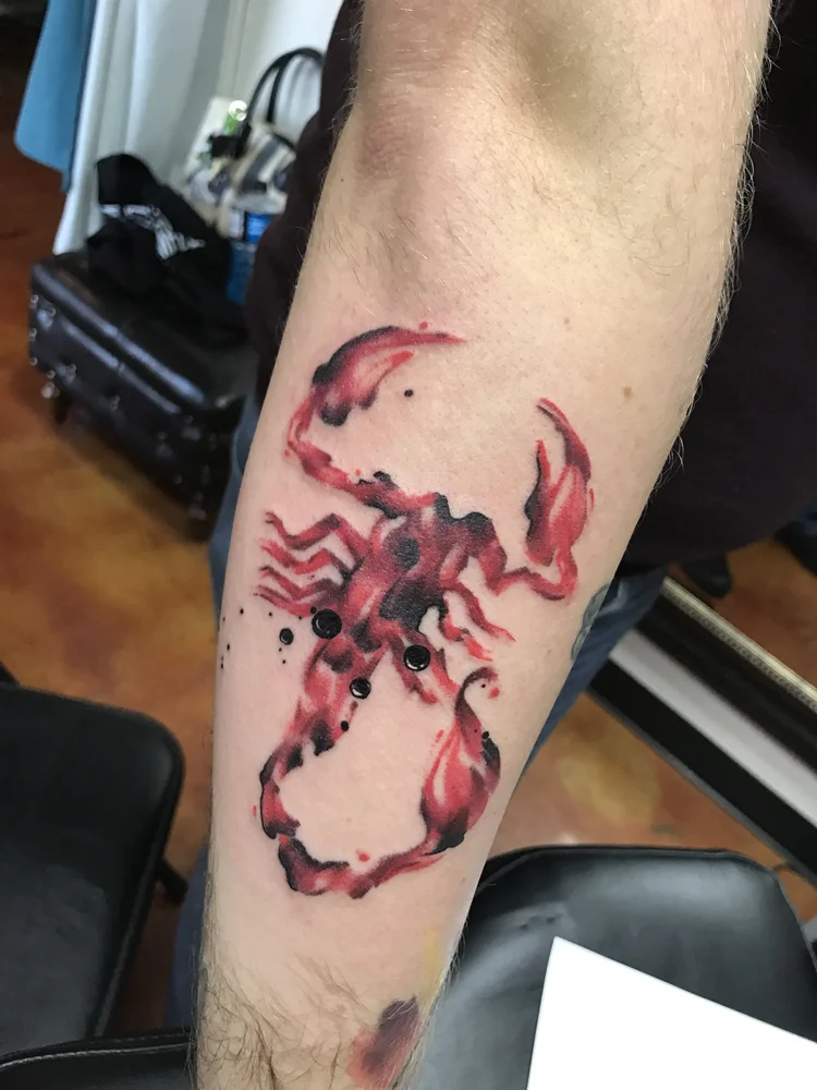 Red watercolor scorpion on the forearm